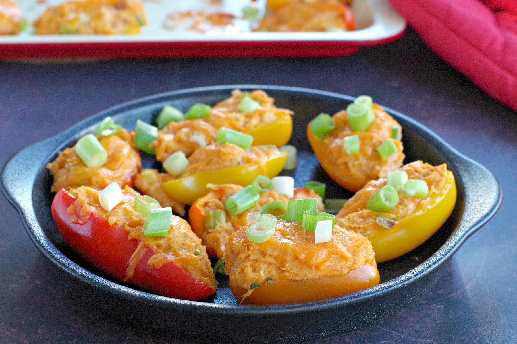 healthy stuffed mini peppers on a black appetizer tray with baking sheet in the background