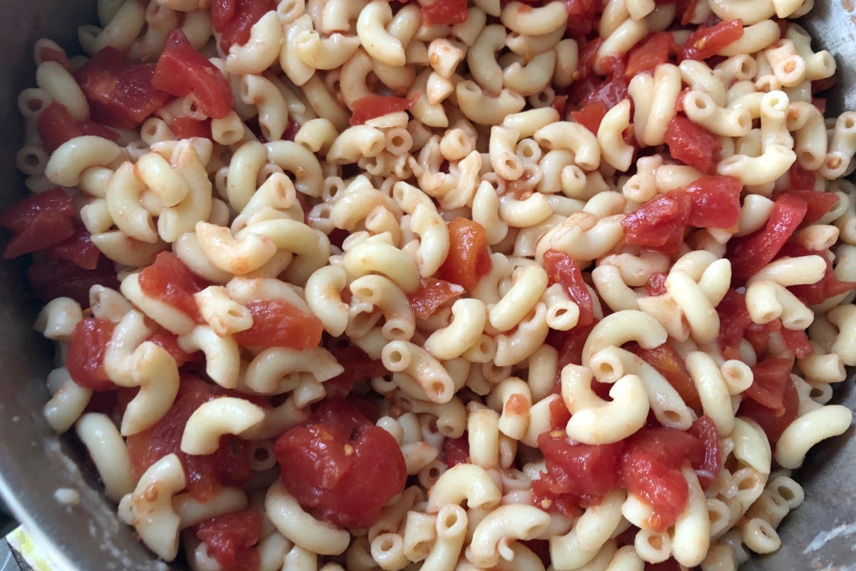 Tomatoes being mixed with macaroni