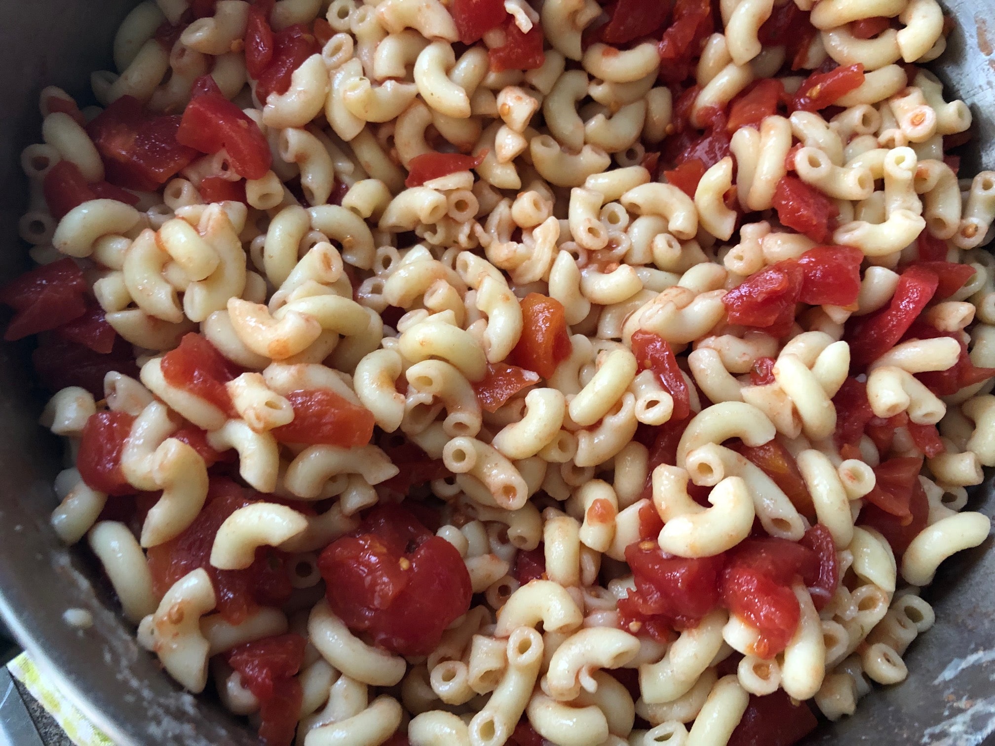 Tomatoes being mixed with macaroni