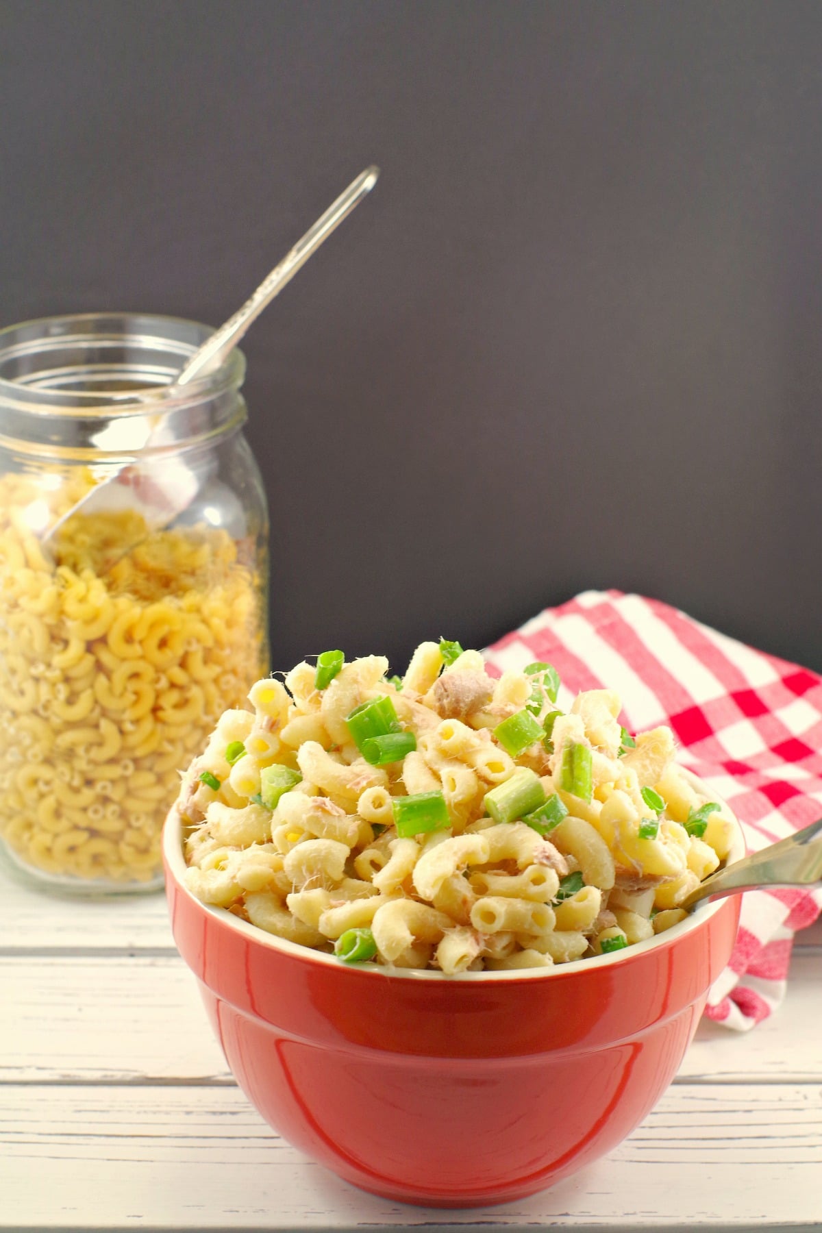 Macaroni salad in red bowl with uncooked macaroni in background