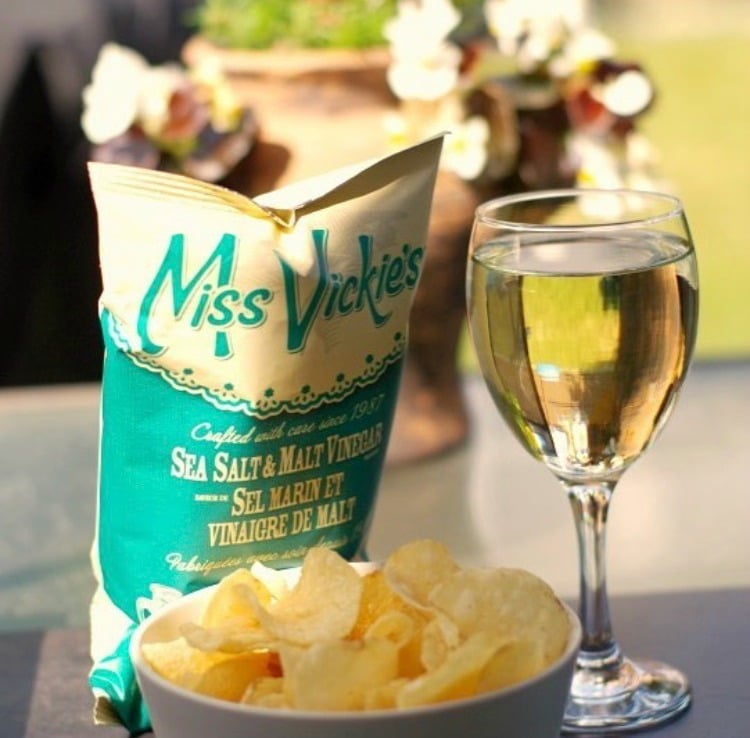 glass of wine with bowl of chips and chip bag behind it