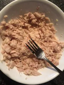 canned chicken being broken up with fork in a white bowl