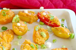 stuffed mini peppers on an off-white baking sheet with red oven mitts in the background