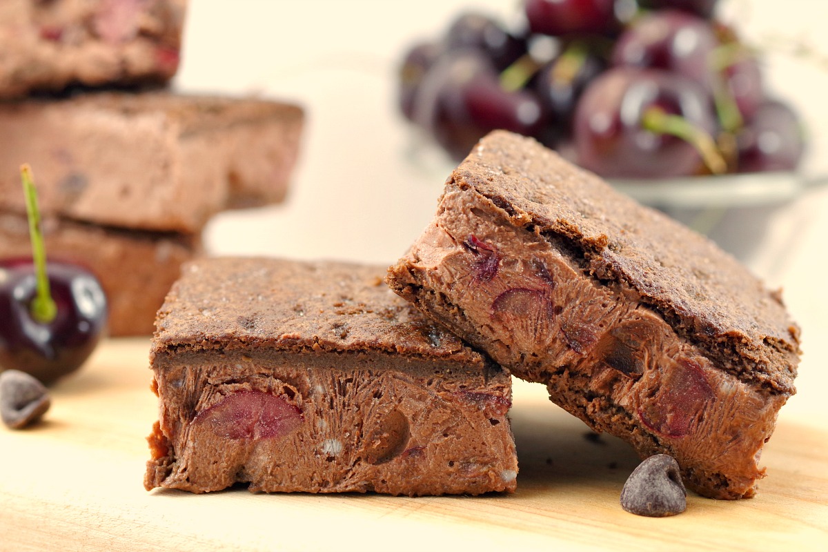 2 black forest ice cream sandwiches on cutting board with cherries in background