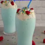 2 blue raspberry slushie drinks on grey counter with sprinkles and raspberries