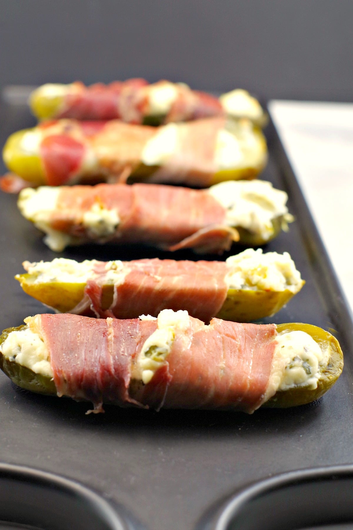 Prosciutto wrapped boursin stuffed pickles on a black tray