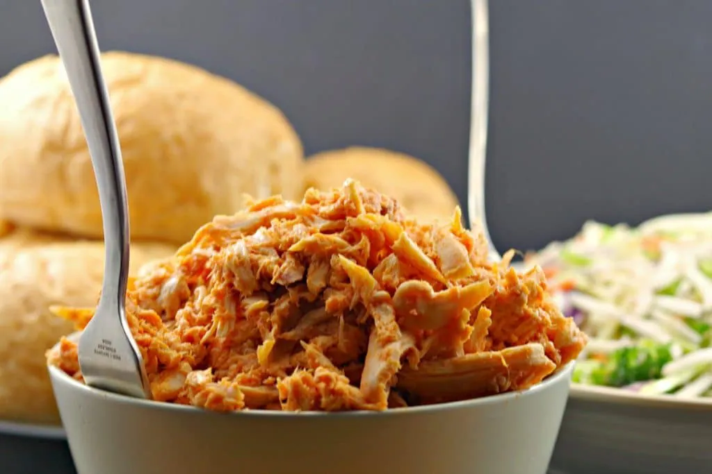 Bowl of buffalo pulled chicken with buns in the background