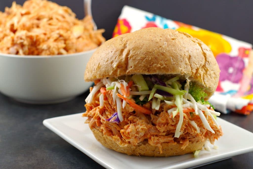 Buffalo Chicken Sandwich on white plate with bowl of shredded buffalo chicken in background