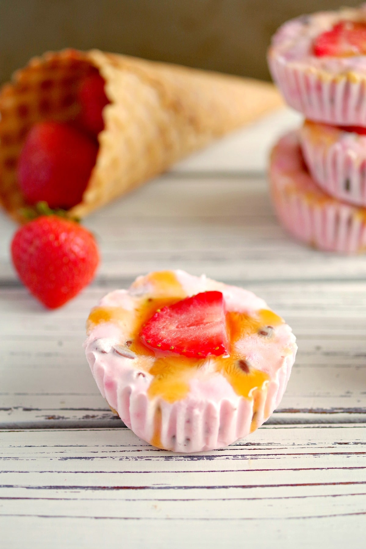 Strawberry Drumstick Frozen Yogurt Cups on white table with strawberries and cones in background