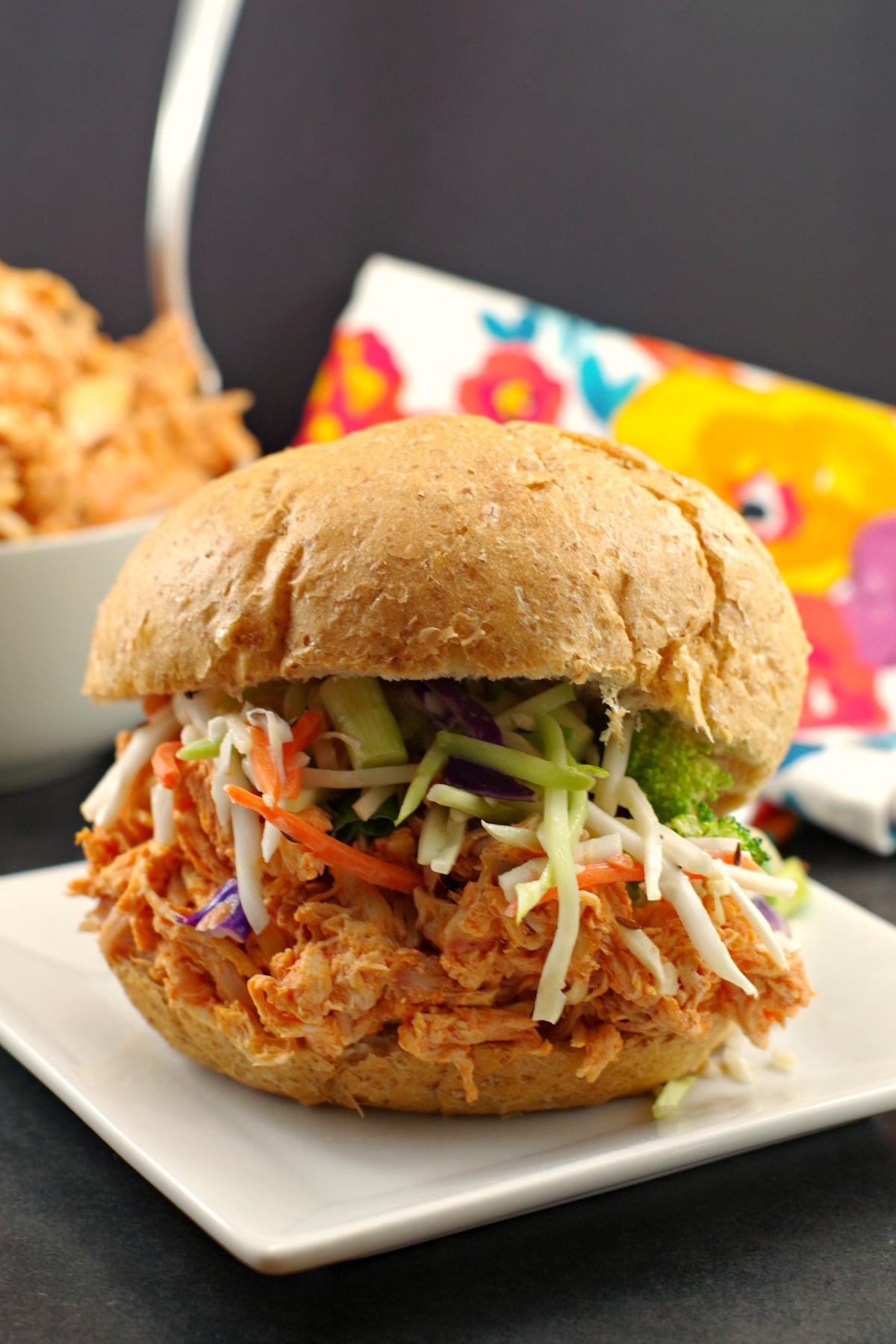 Buffalo Chicken Sandwich on white plate with bowl of shredded buffalo chicken in background