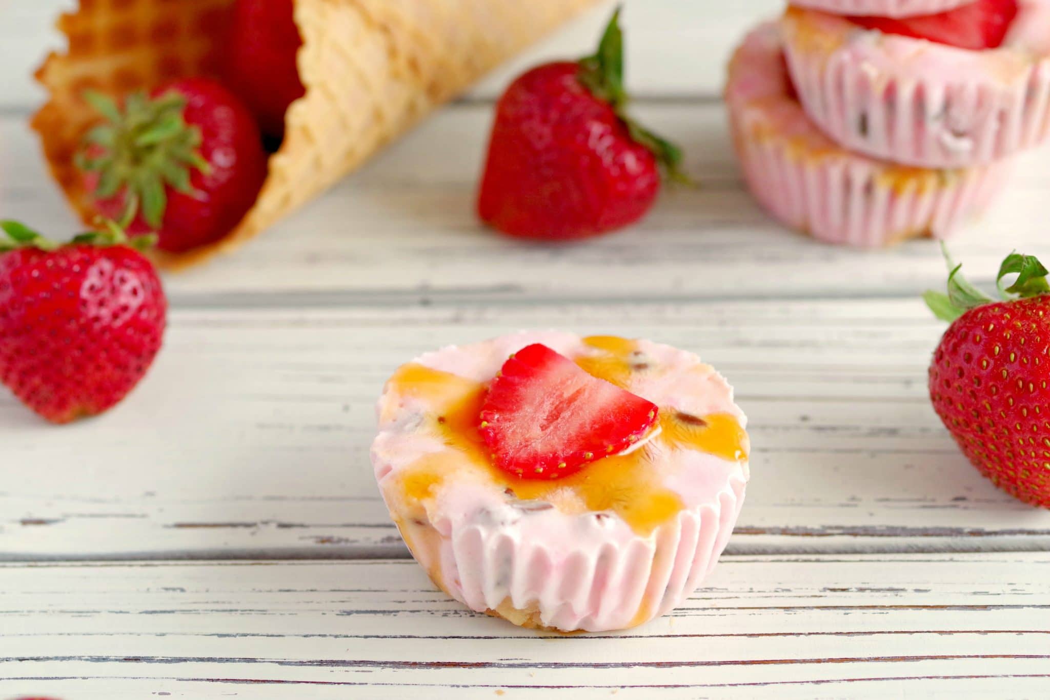 Strawberry Drumstick Frozen Yogurt Cups on white table with strawberries and cones in background