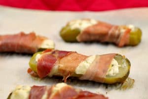 Prosciutto wrapped boursin stuffed pickle on a parchment covered sheet pan