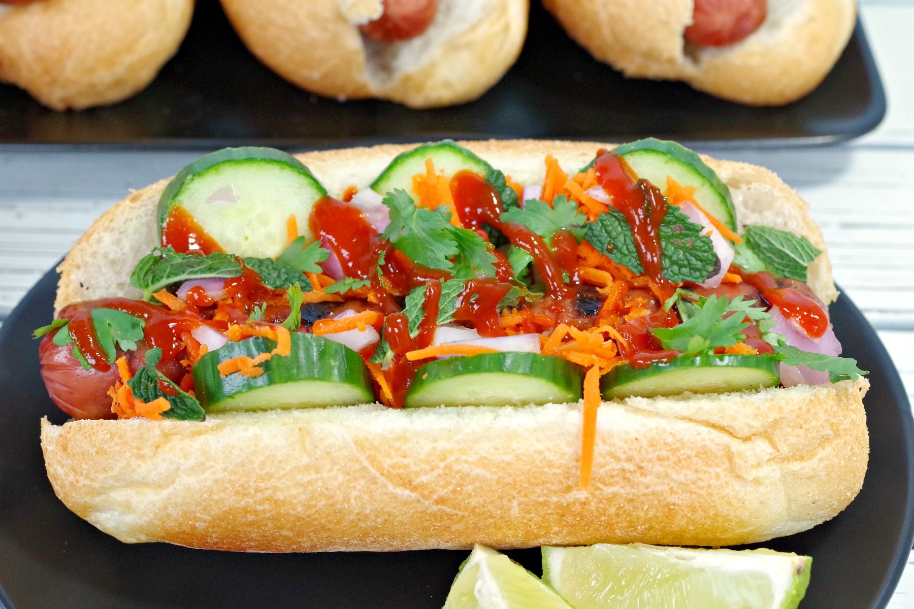 Side view of Banh Mi Turkey Hot dog on black plate with lime wedges