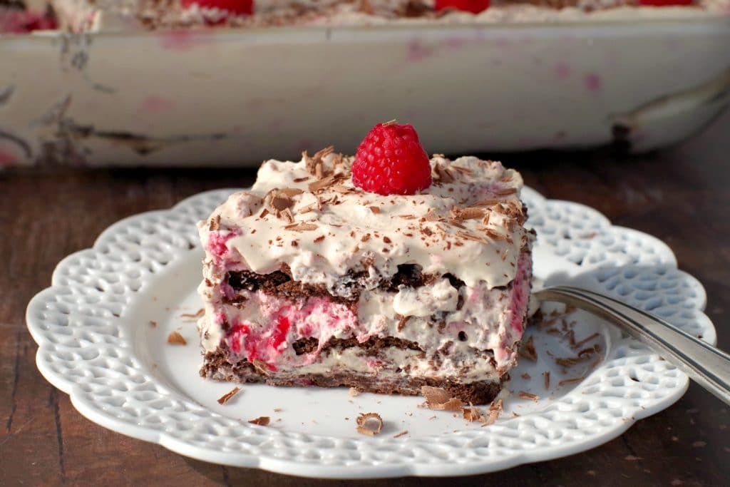 A piece of raspberry dulce de leche icebox cake on an elegant white plate with cake in background