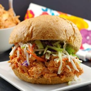 rotisserie chicken sandwich on a white plate with shredded chicken in background