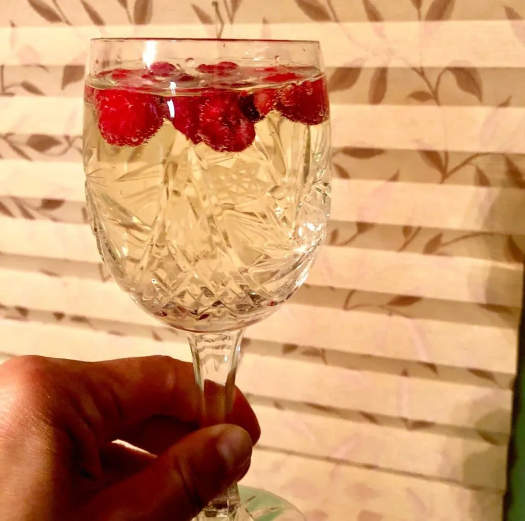 Glass of white wine with frozen raspberries as ice cubes