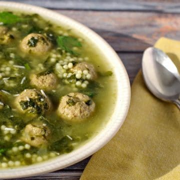 Easy Italian wedding soup with frozen meatballs on a bluish wooden background with a yellow napkin and spoon