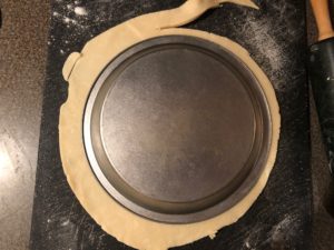 Pie crust with pie plate on top, being trimmed