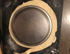 Pie crust with pie plate on top, being trimmed