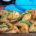 cornish game hens with rosemary wine sauce in a glass dish with blue oven mitts in background