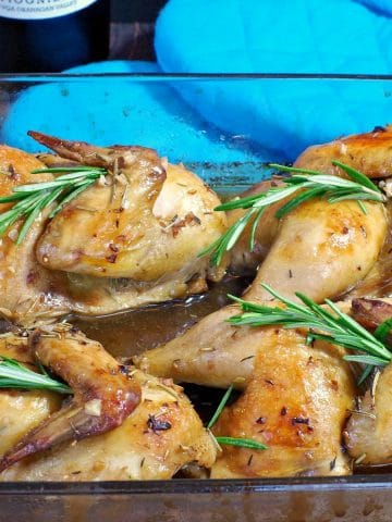 cornish game hens with rosemary wine sauce in a glass dish with blue oven mitts in background
