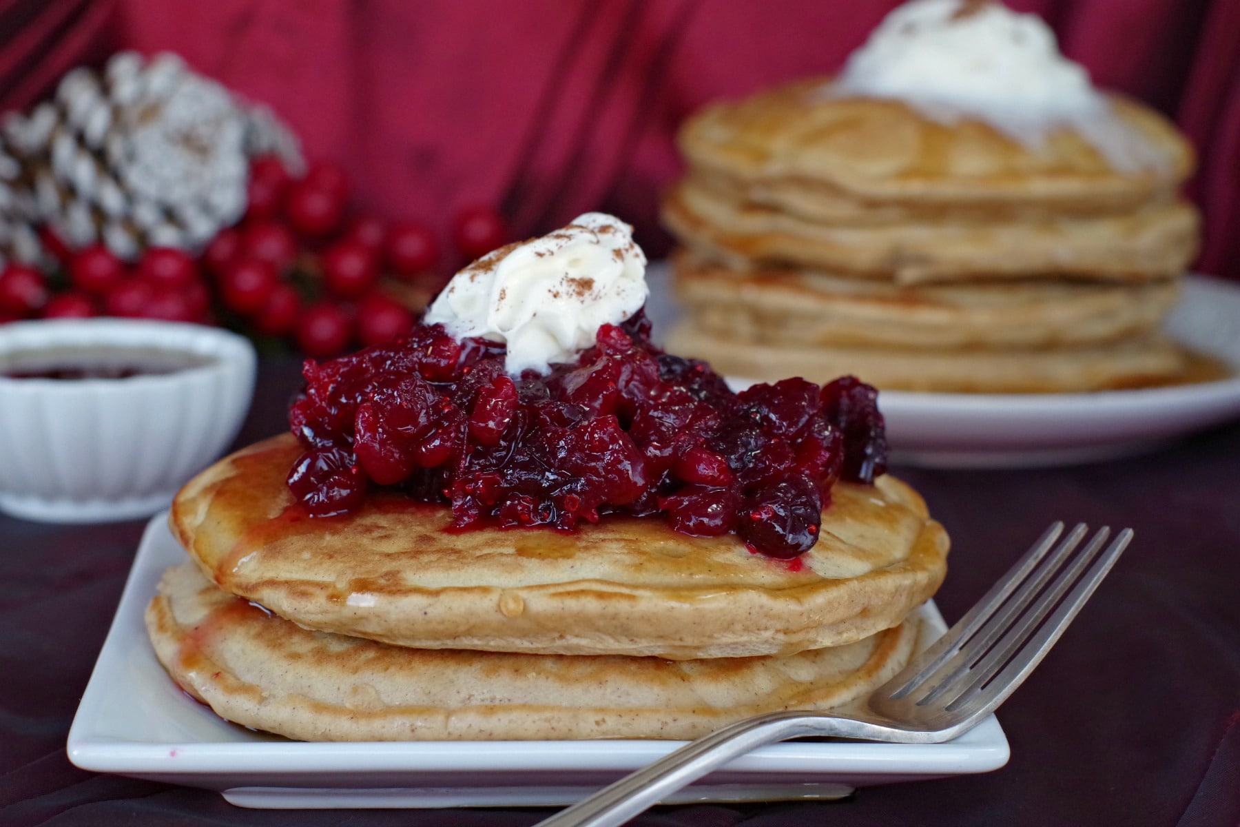2 gingerbread pancakes with cranberry compote and stack of gingerbread pancakes in the background