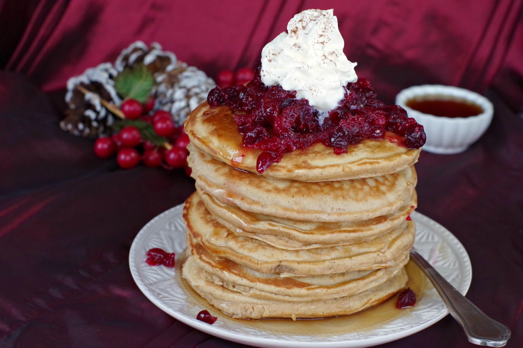 stack of gingerbread pancakes with cranberry compote and whipped cream on top