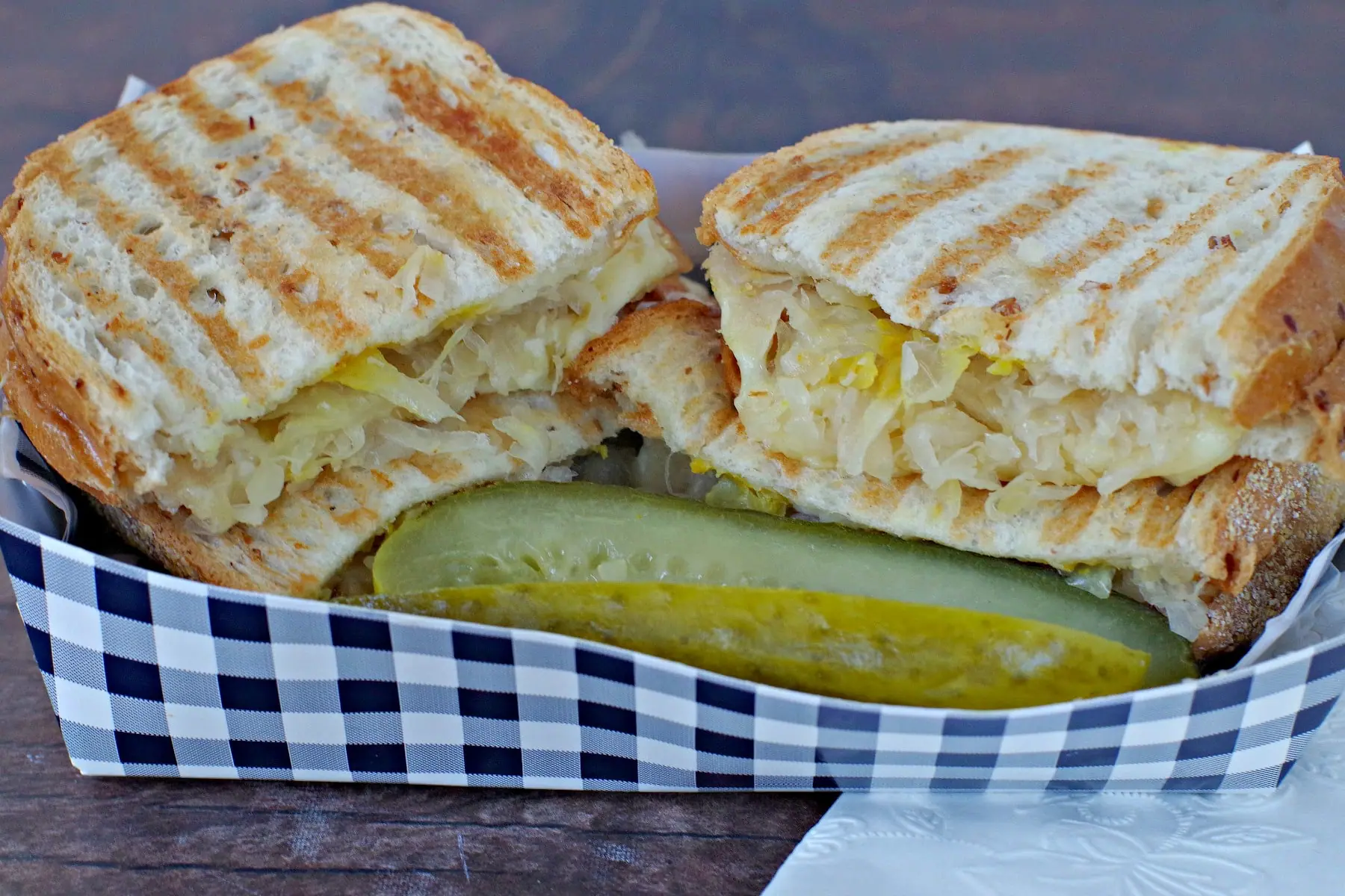 Turkey Reuben sliced in half in a paper blue checkered box with a pickle in front