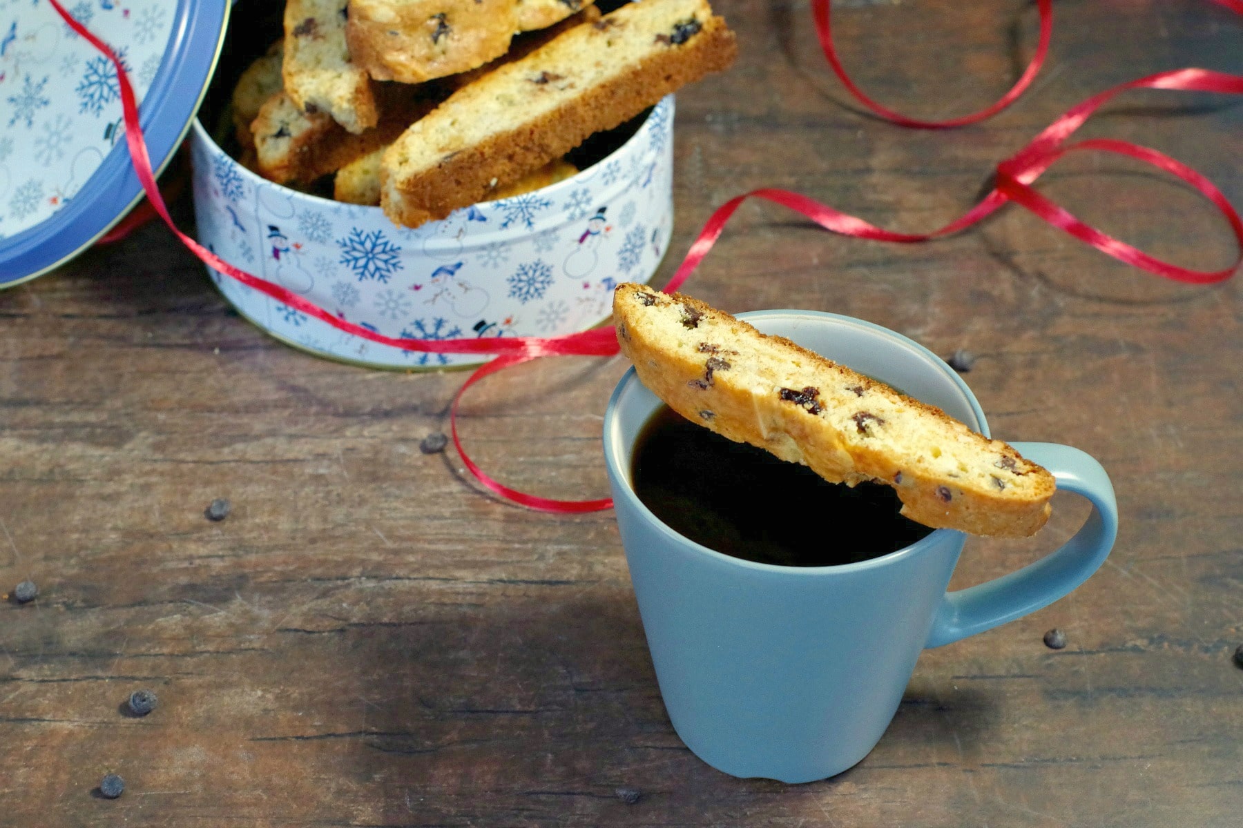 Black forest biscotti on a blue mug with Christmas tin of more biscotti in background