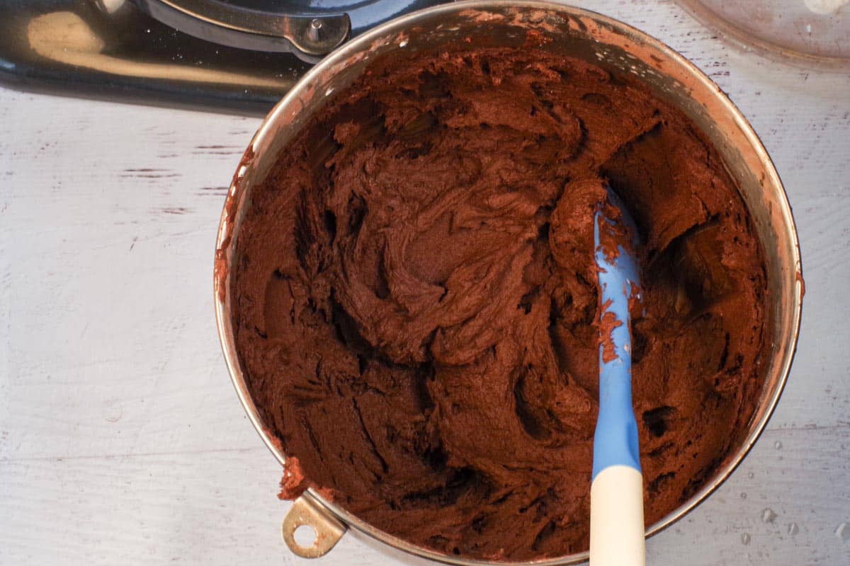 frosting beaten until it's a smooth texture in a stand mixer bowl with blue and white spatula