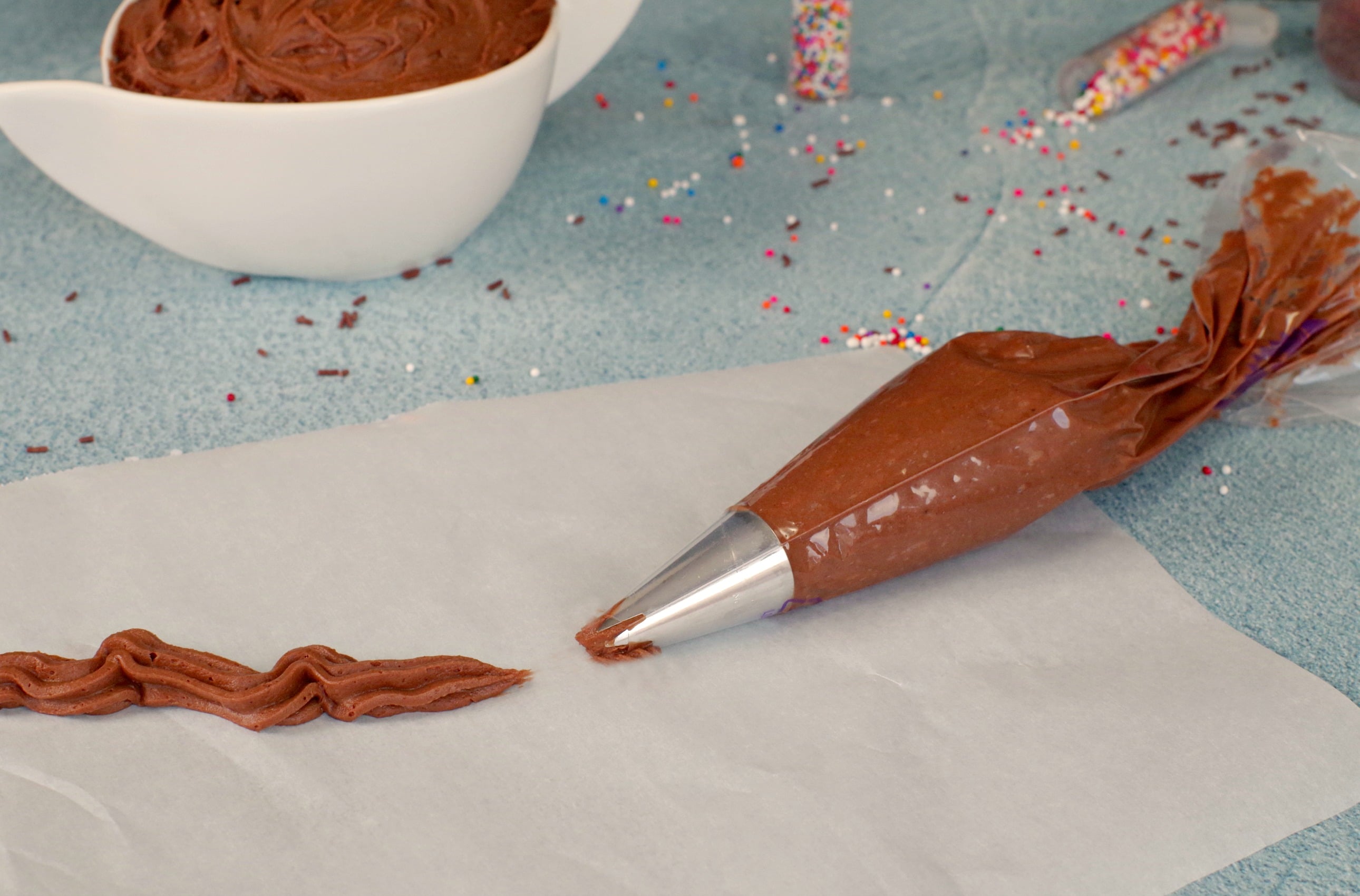 Chocolate frosting in pastry bag on parchment paper with line of frosting on top