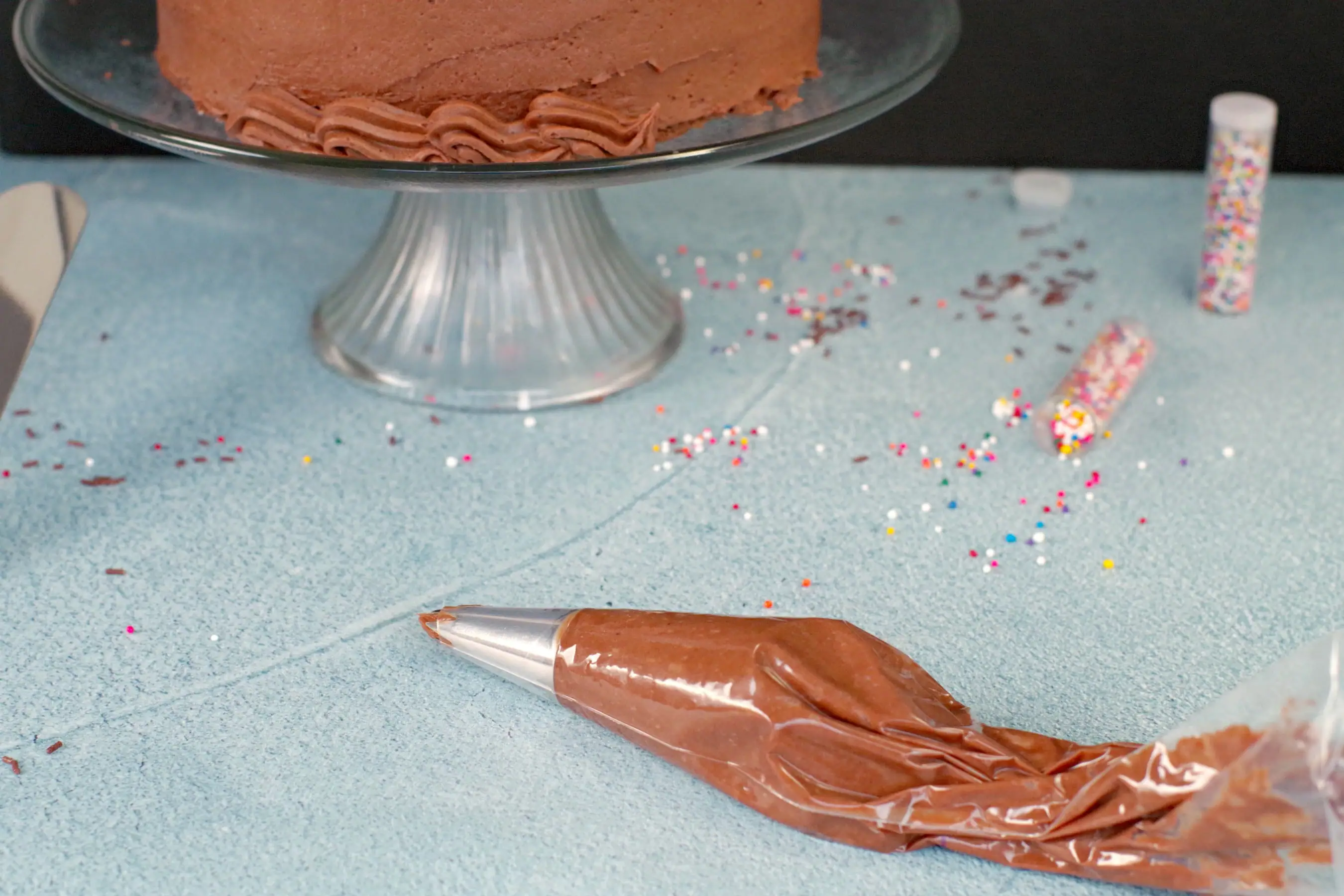 Chocolate frosting in pastry bag with partially decorated cake in the background