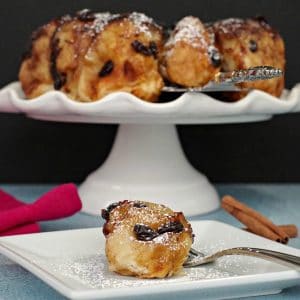 cinnamon sticky buns on a white cake stand in background, with a single bun on a white plate in front