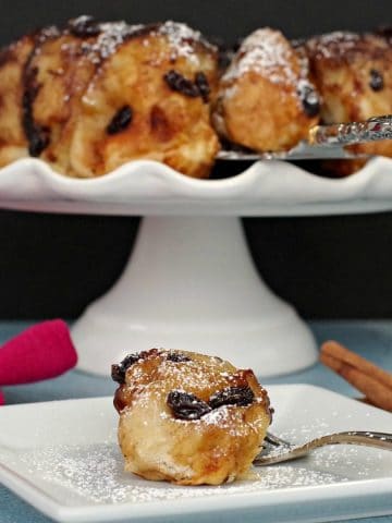 cinnamon sticky buns on a white cake stand in background, with a single bun on a white plate in front