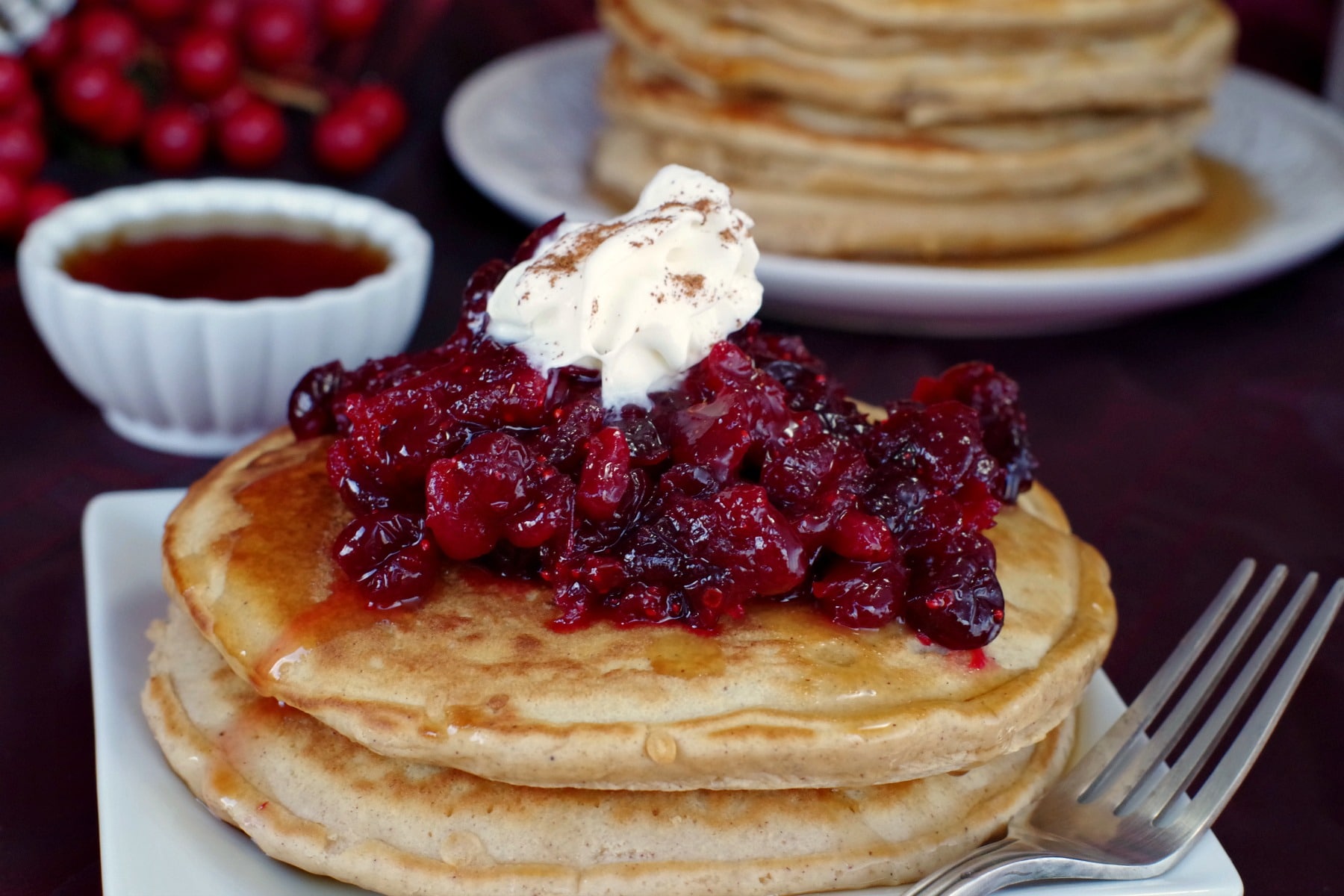 2 gingerbread pancakes with cranberry compote and stack of gingerbread pancakes in the background