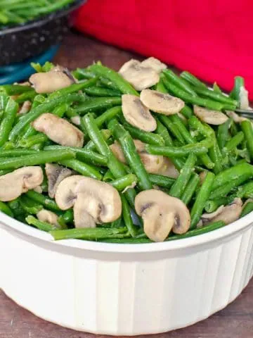green beans and mushrooms in a white casserole dish on brown surface with red oven mitt in background