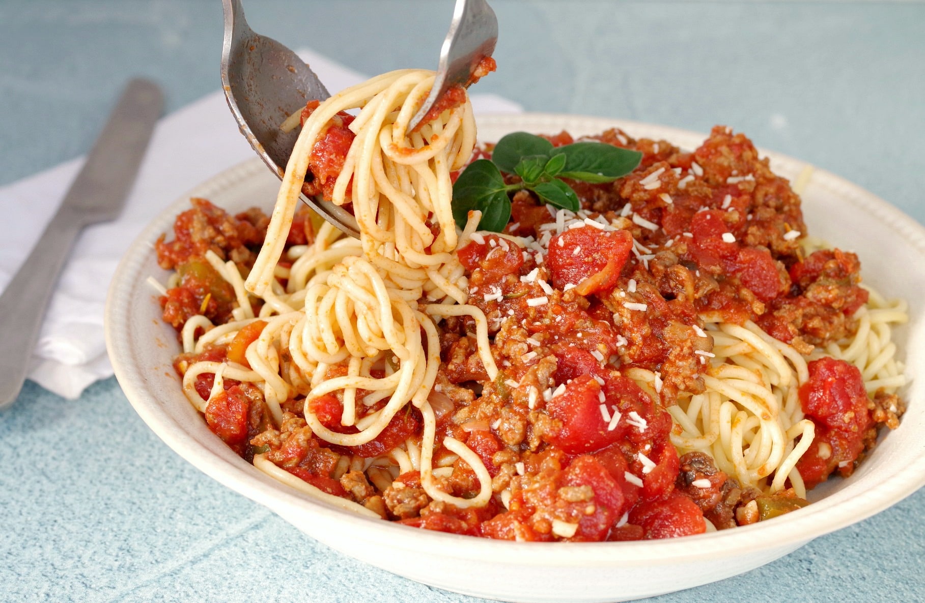 Spaghetti and meat sauce with spaghetti being twirled on fork with spoon