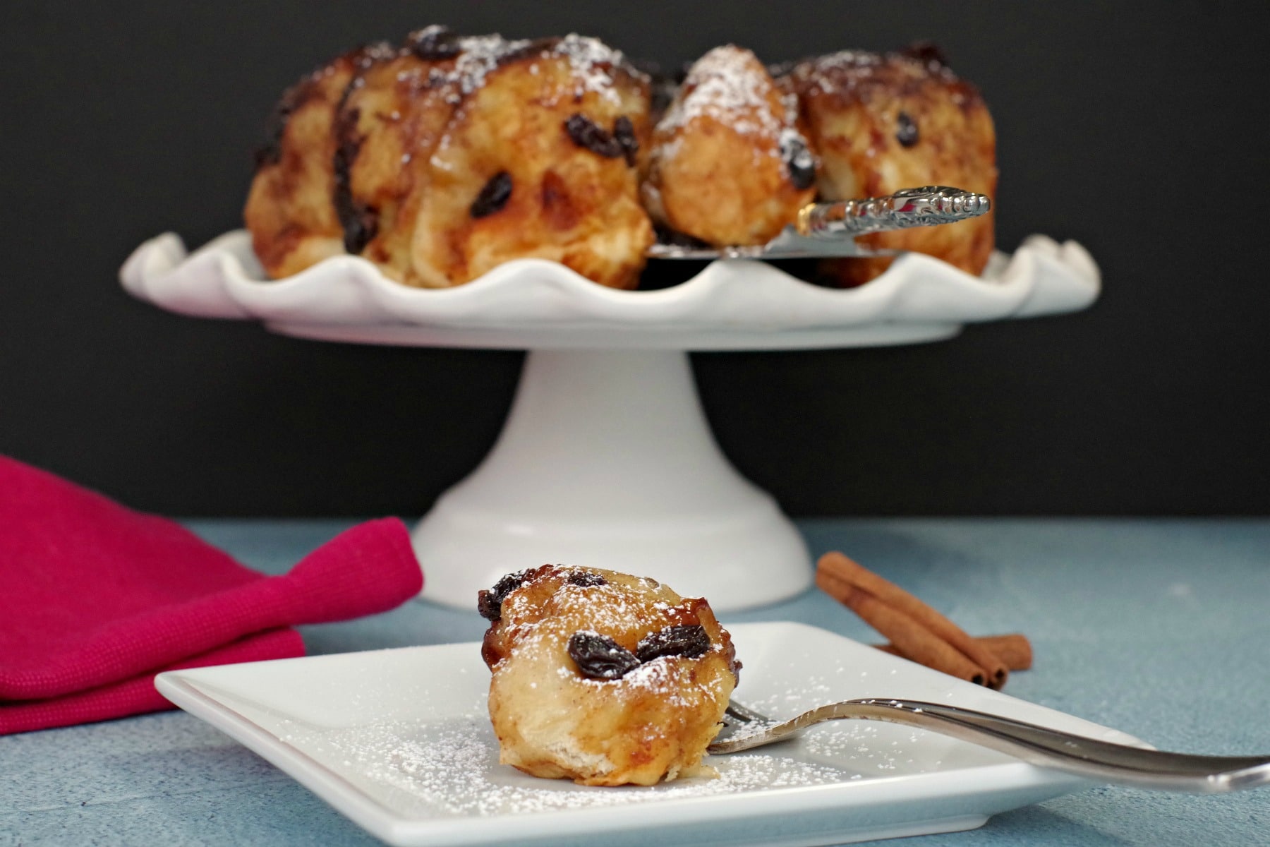 Overnight Cinnamon Sticky Buns on a white cake platter with bun on white plate in front