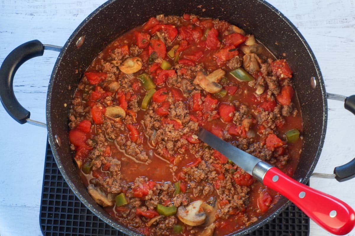 spaghetti sauce with ground beef added in large pot with a spoon