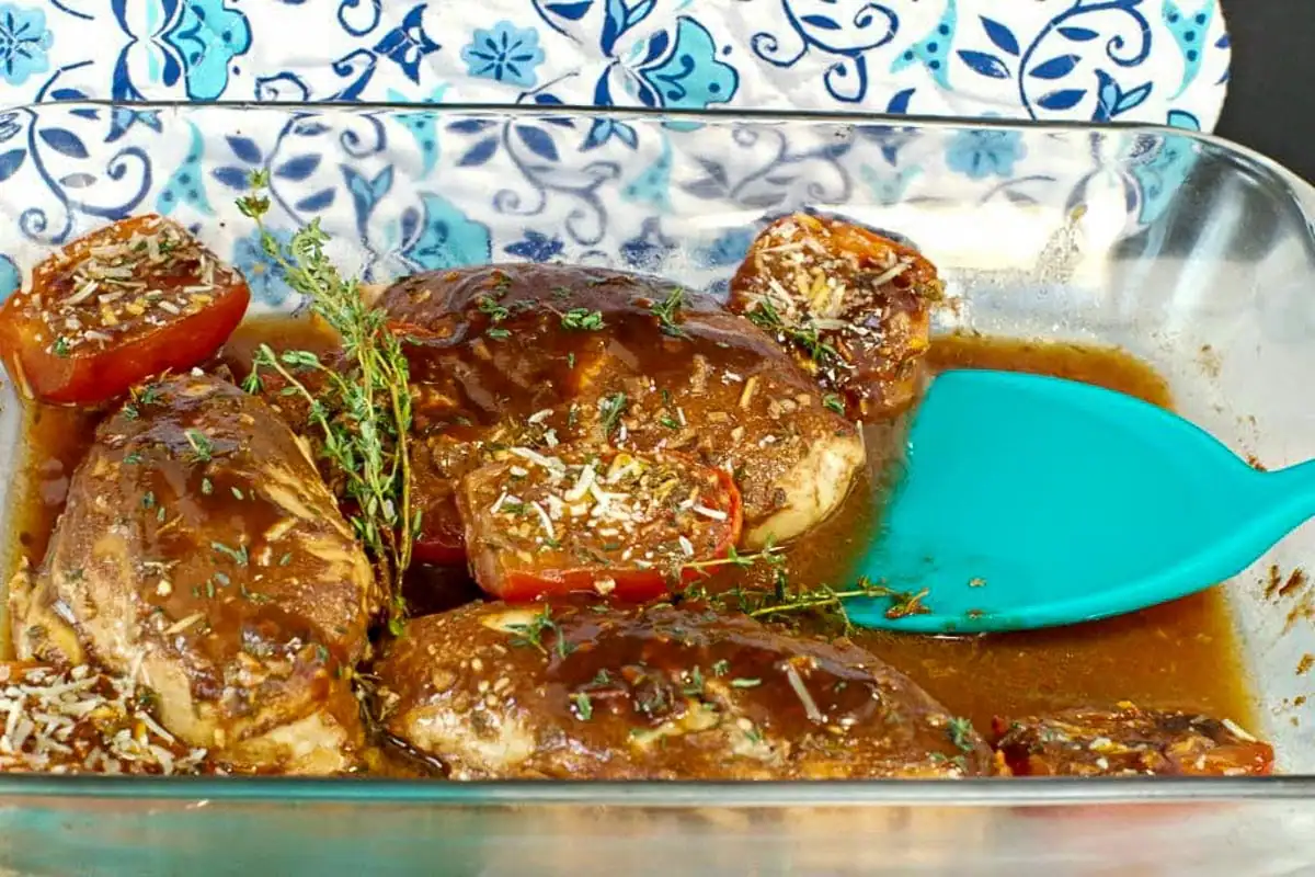 Balsamic chicken with tomatoes in a glass dish with an aqua blue spatula