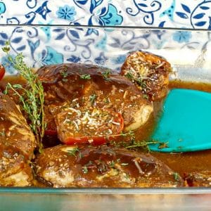 Balsamic chicken with tomatoes in a glass dish with aqua blue spatula