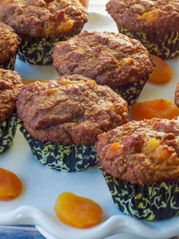 healthy bran pumpkin muffins on a white cake platter with dried apricots