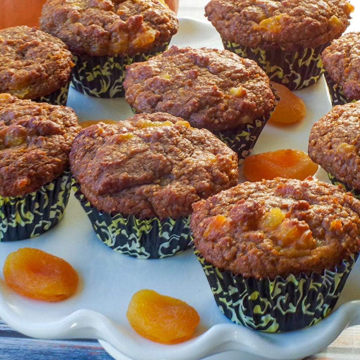 healthy bran pumpkin muffins on a white cake platter with dried apricots