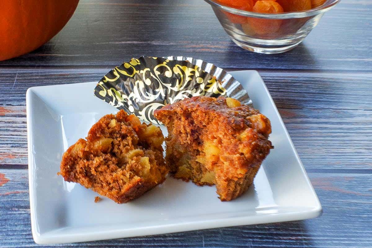 Healthy bran pumpkin muffin split in half,  on a white plate with a muffin liner