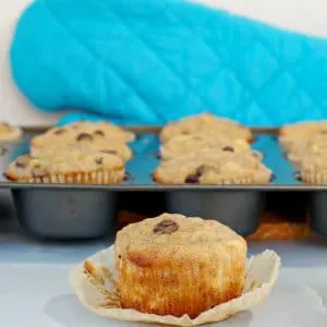 healthy chocolate chip banana muffins in muffin tin in background, with muffin on wrapper in front
