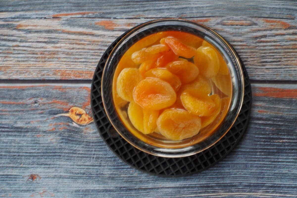 Dried apricots soaking in hot water in a small glass bowl on trivet