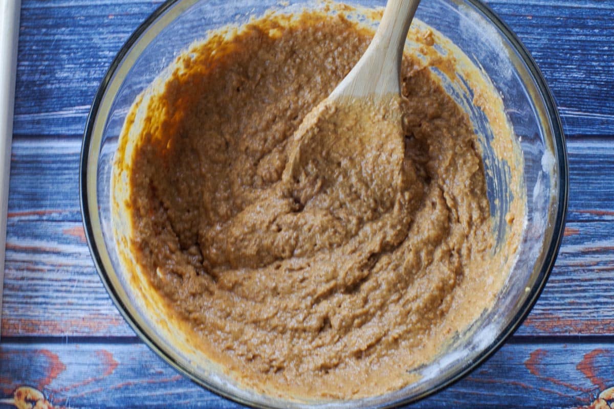 wet and dry ingredients mixed together in a large glass bowl with wooden spoon