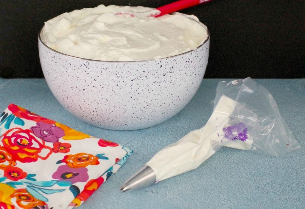 Whipped cream frosting in bowl with filled pastry bag in front