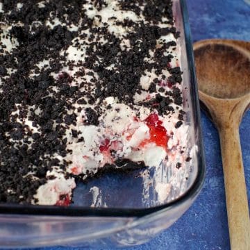 cherry cha cha dessert in glass container, with some scooped out and wooden spoon on right hand side (all on blue background)