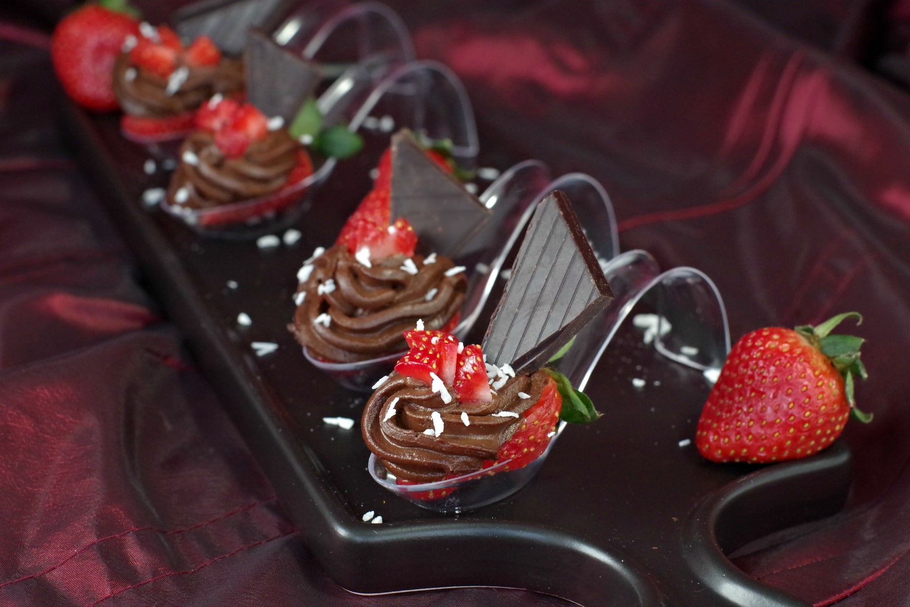 4 Chocolate Avocado strawberry desserts on spoons on a black appetizer tray